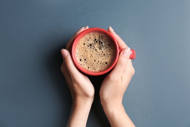 Young woman with cup of delicious hot coffee on grey background, top view