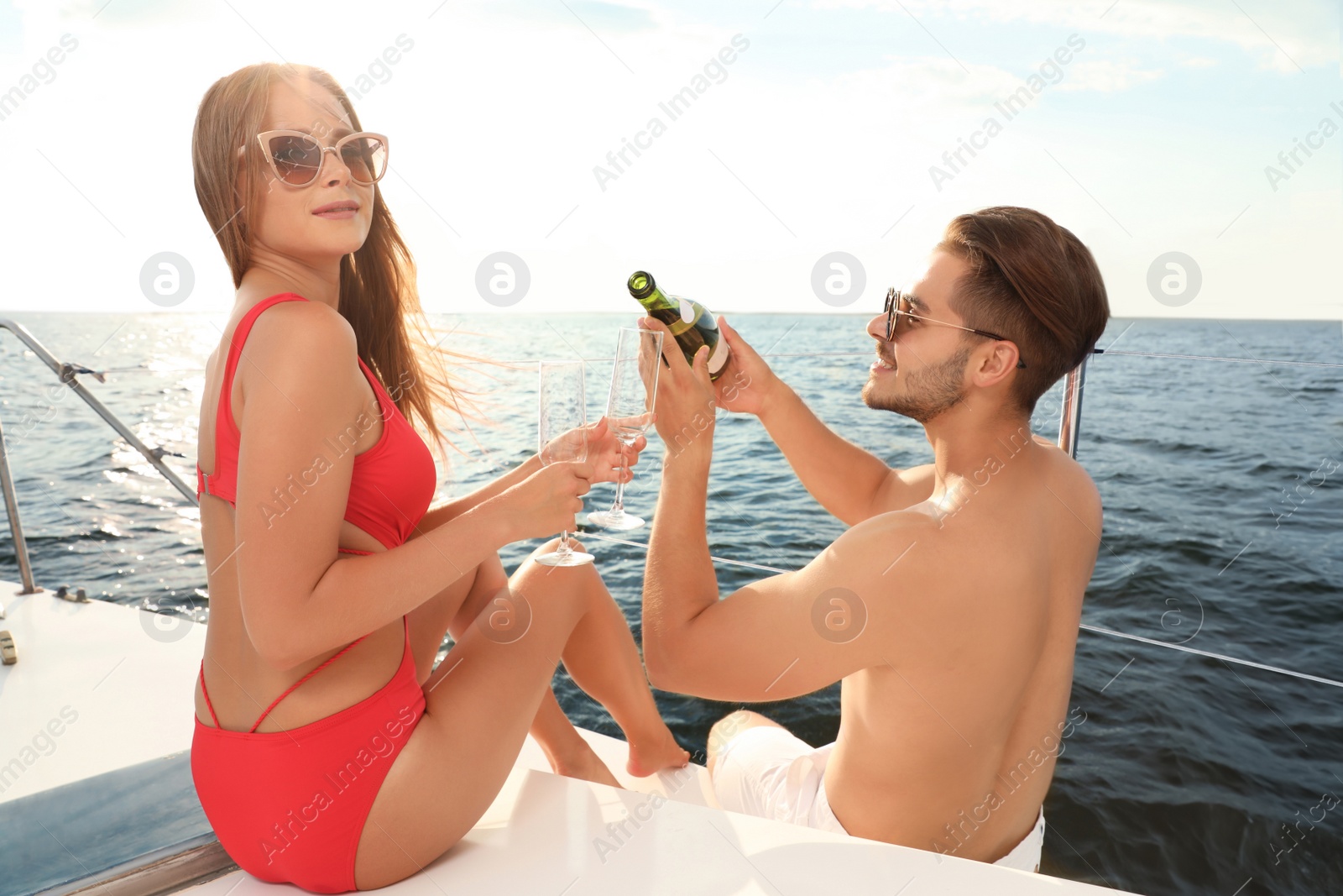 Photo of Young man and his girlfriend in bikini drinking champagne on yacht. Happy couple on vacation