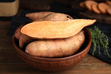 Photo of Cut and whole sweet potatoes in bowl on wooden table, closeup