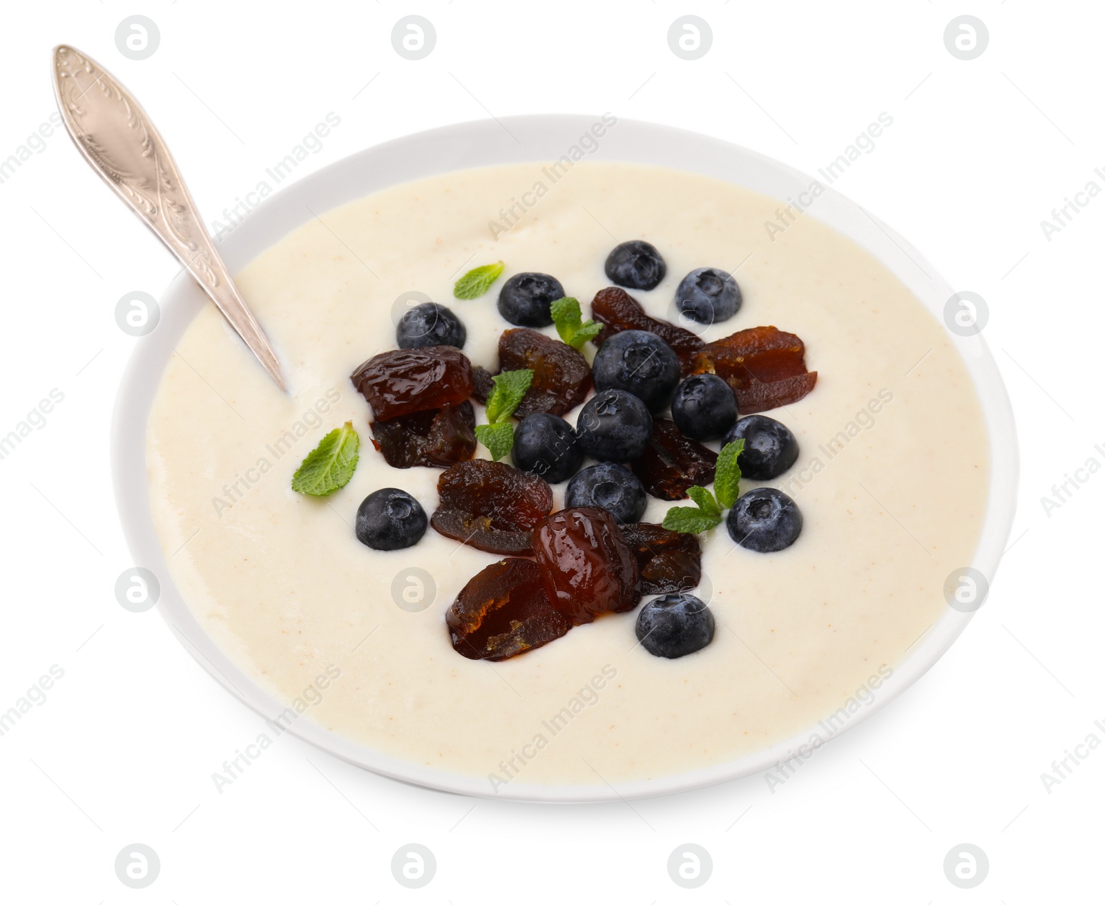 Photo of Delicious semolina pudding with blueberries, dates, mint and spoon in bowl isolated on white