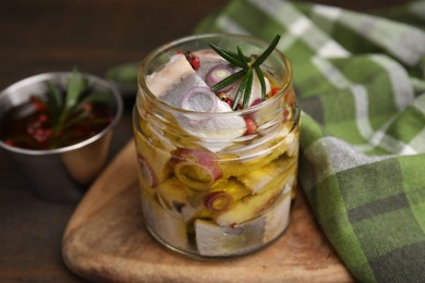 Tasty marinated fish with onion and rosemary in jar on wooden table, closeup