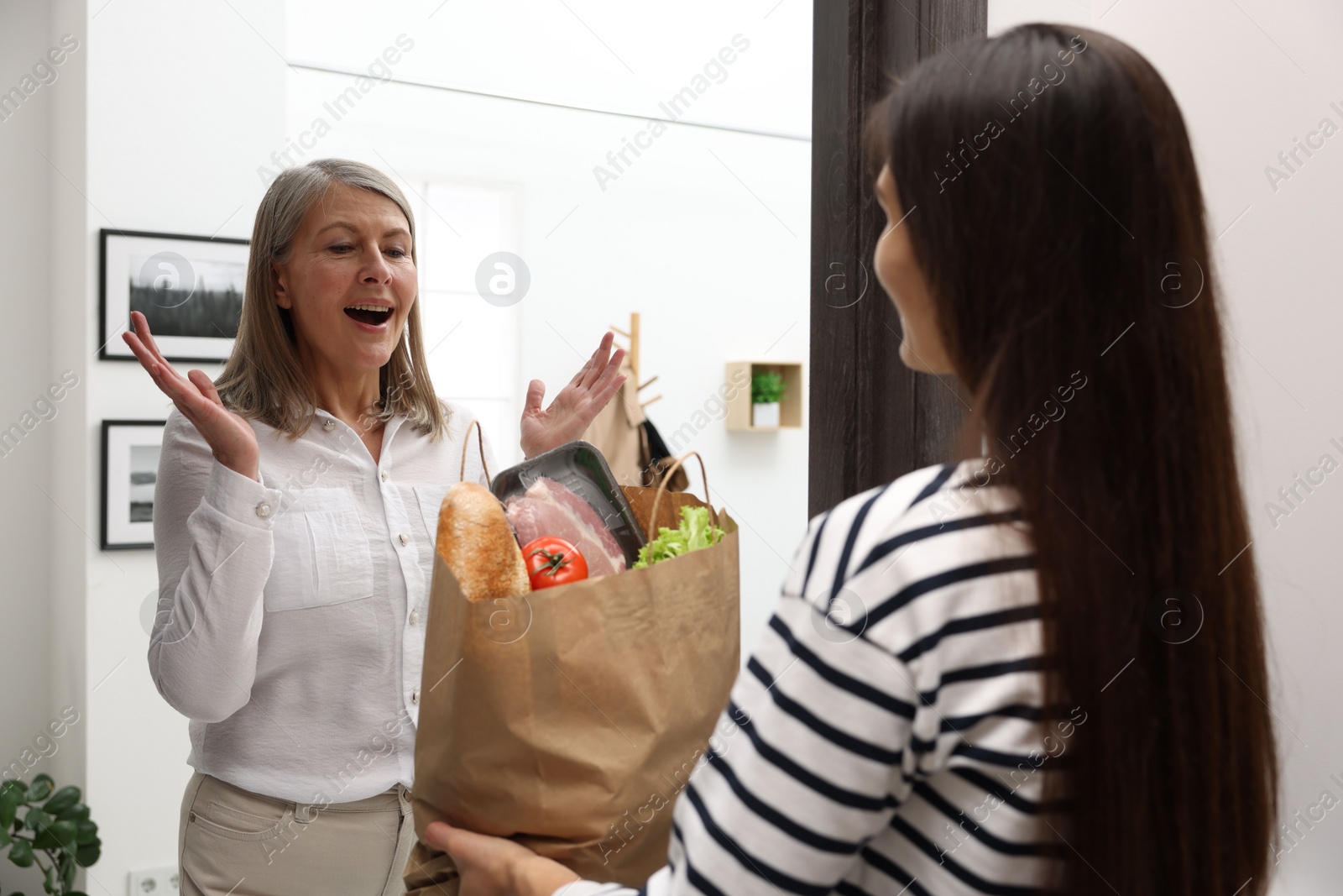 Photo of Courier giving paper bag with food products to senior woman indoors