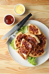 Photo of Tasty Belgian waffles served with bacon, lettuce and sauces on wooden table, flat lay