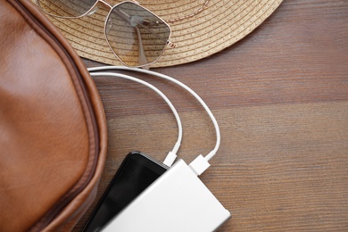 Photo of Charging mobile phone with power bank and backpack on wooden table, flat lay