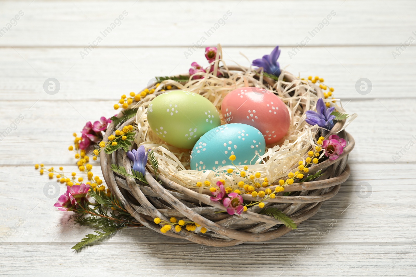 Photo of Wicker nest with painted Easter eggs and flowers on wooden table