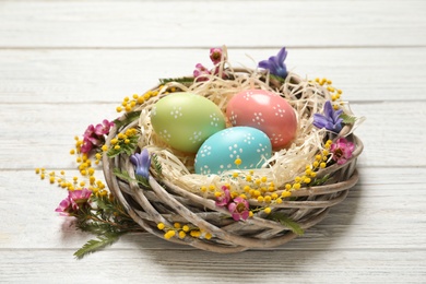 Wicker nest with painted Easter eggs and flowers on wooden table