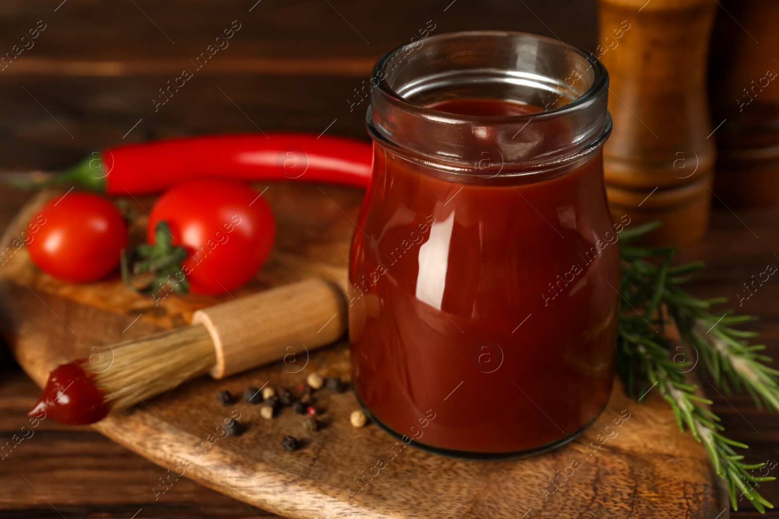 Photo of Tasty barbecue sauce in glass jar, brush and ingredients on wooden table, closeup