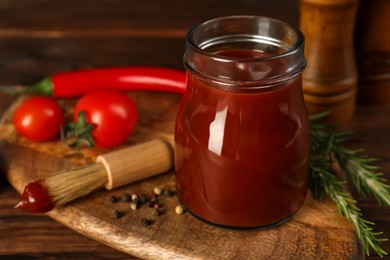 Tasty barbecue sauce in glass jar, brush and ingredients on wooden table, closeup