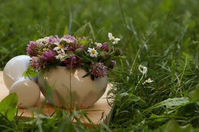 Photo of Ceramic mortar with pestle, different wildflowers and herbs on green grass. Space for text