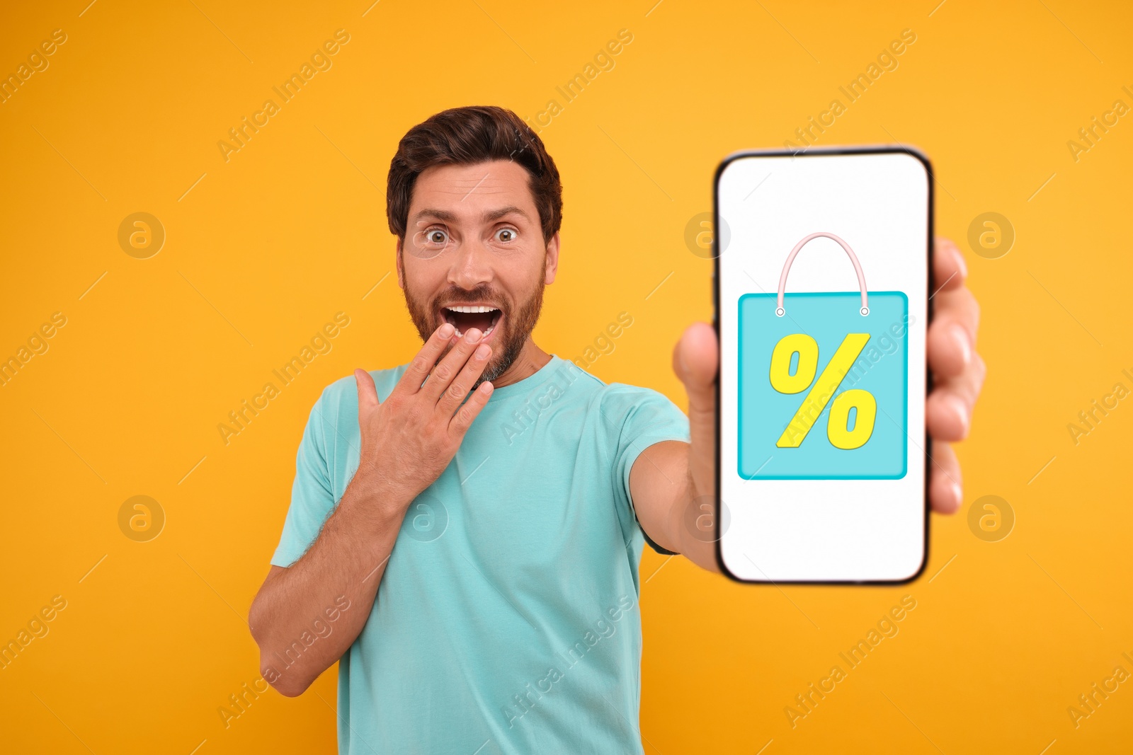 Image of Discount, offer, sale. Emotional man showing mobile phone with illustration of bag and percent sign on screen, orange background