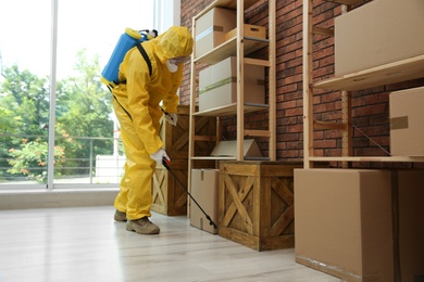 Pest control worker in protective suit spraying pesticide indoors