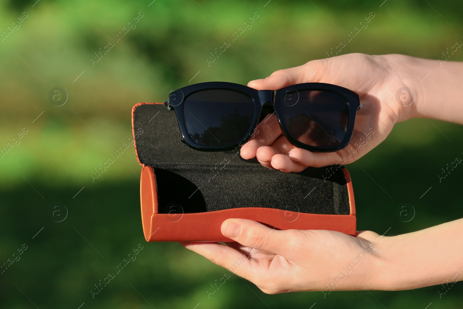 Photo of Woman holding sunglasses and case outdoors on sunny day, closeup