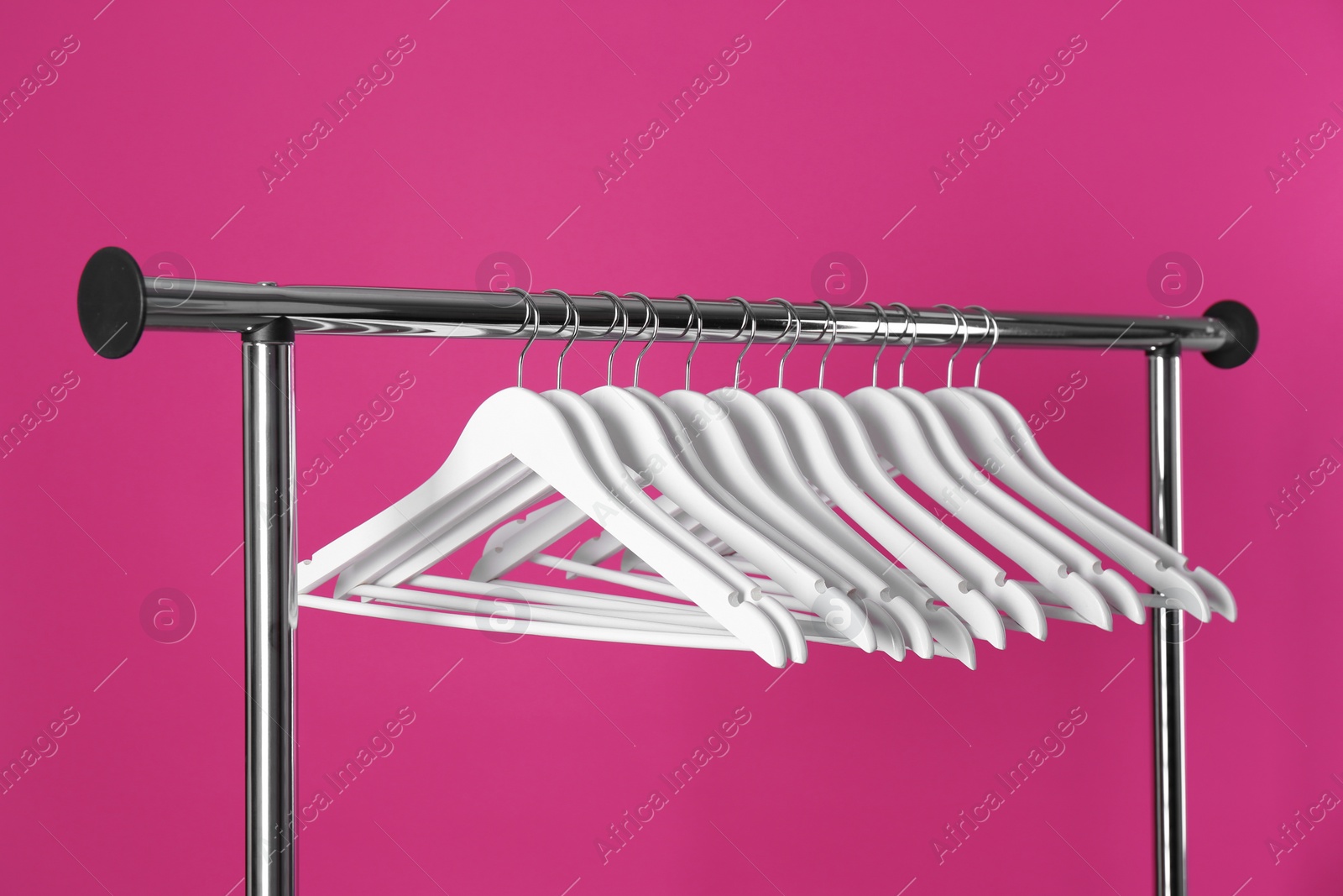 Photo of Metal rack with clothes hangers on color background