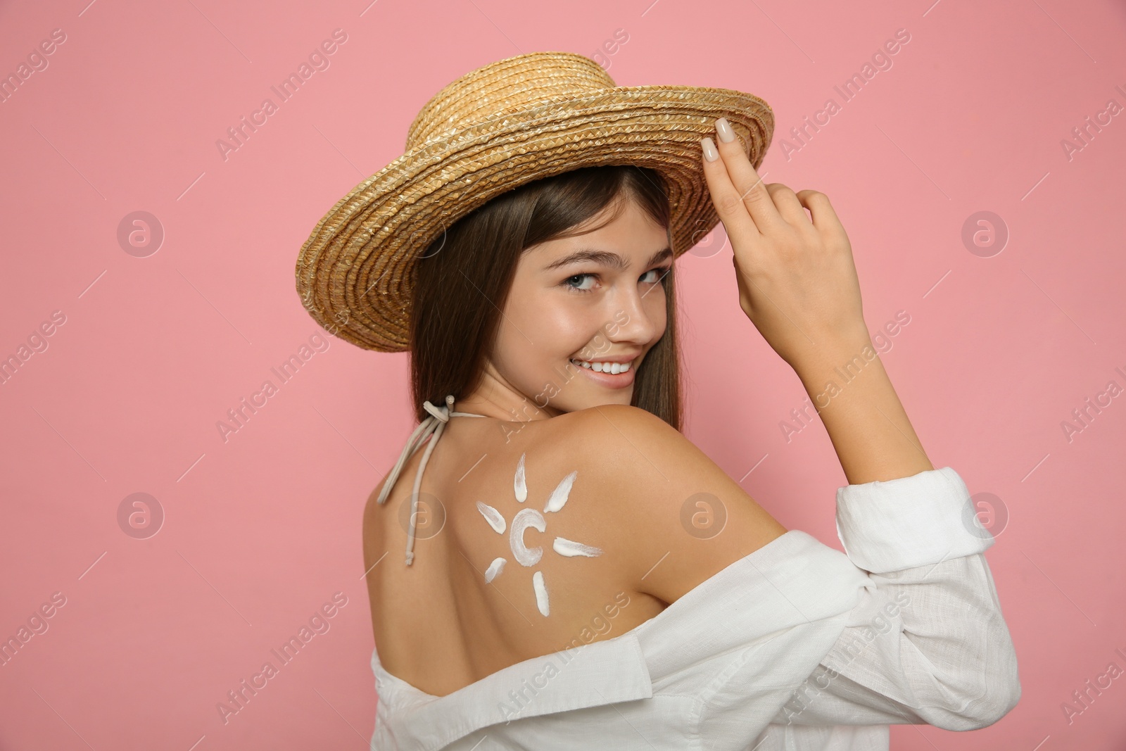 Photo of Teenage girl with sun protection cream on her back against pink background