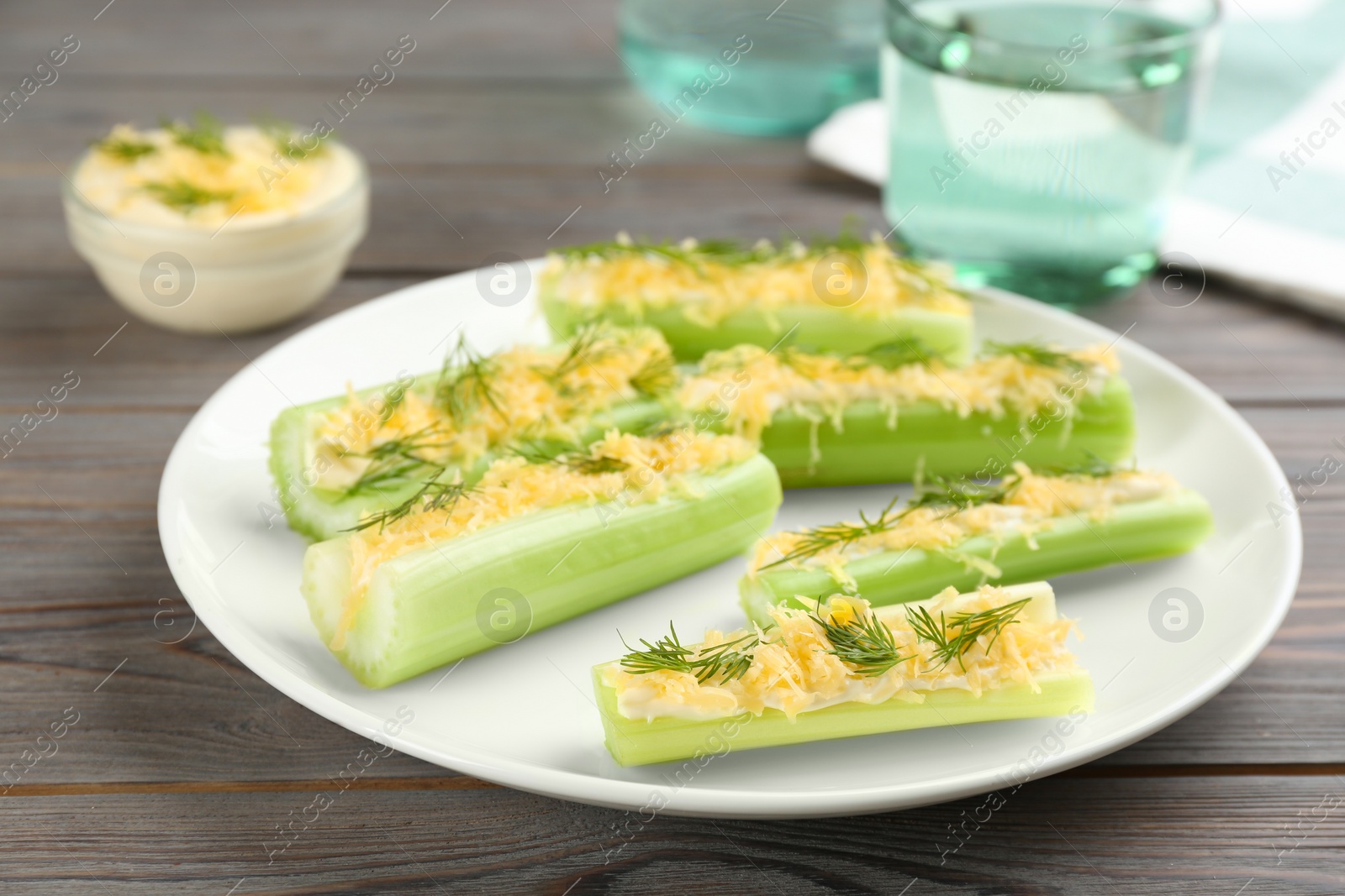 Photo of Celery sticks with sauce, cheese and dill on wooden table