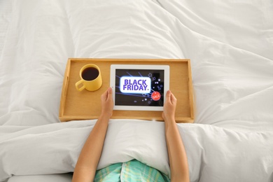 Photo of Woman using tablet with Black Friday announcement while lying in bed, above view