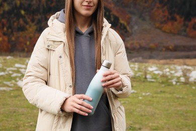 Photo of Woman holding thermo bottle in mountains, closeup