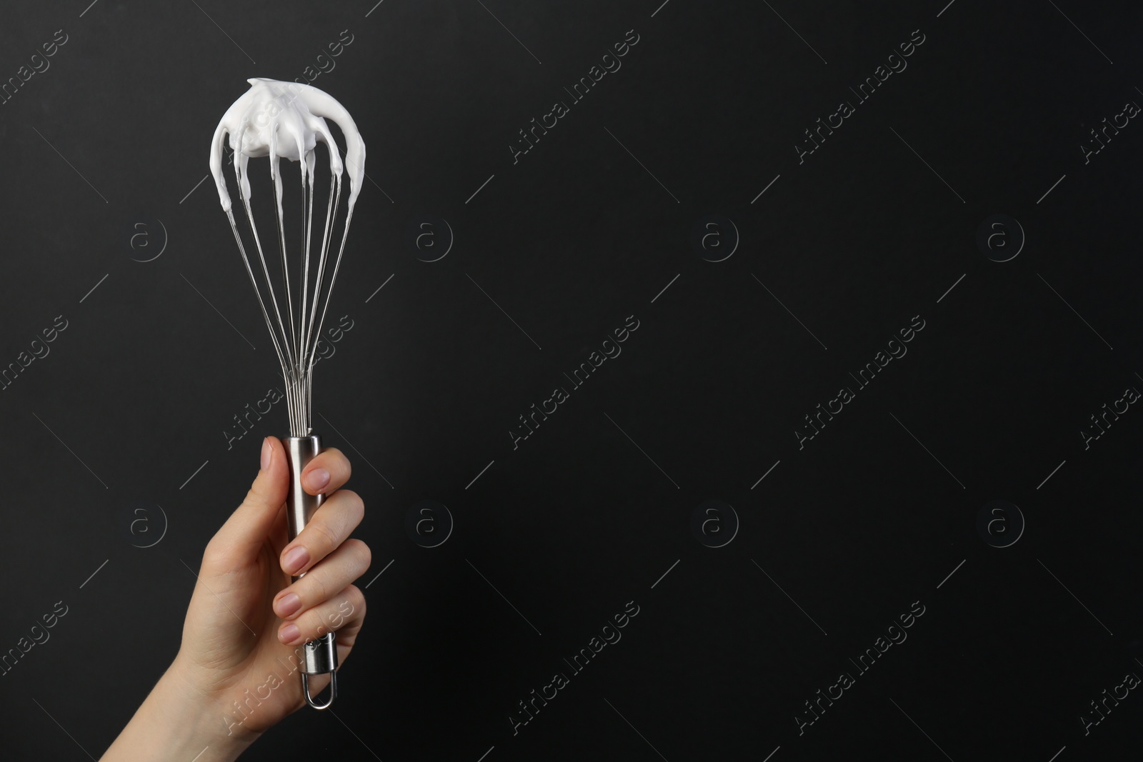 Photo of Woman holding whisk with whipped cream on black background, closeup. Space for text