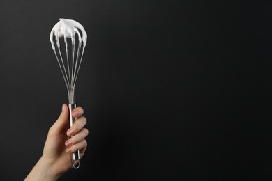 Woman holding whisk with whipped cream on black background, closeup. Space for text