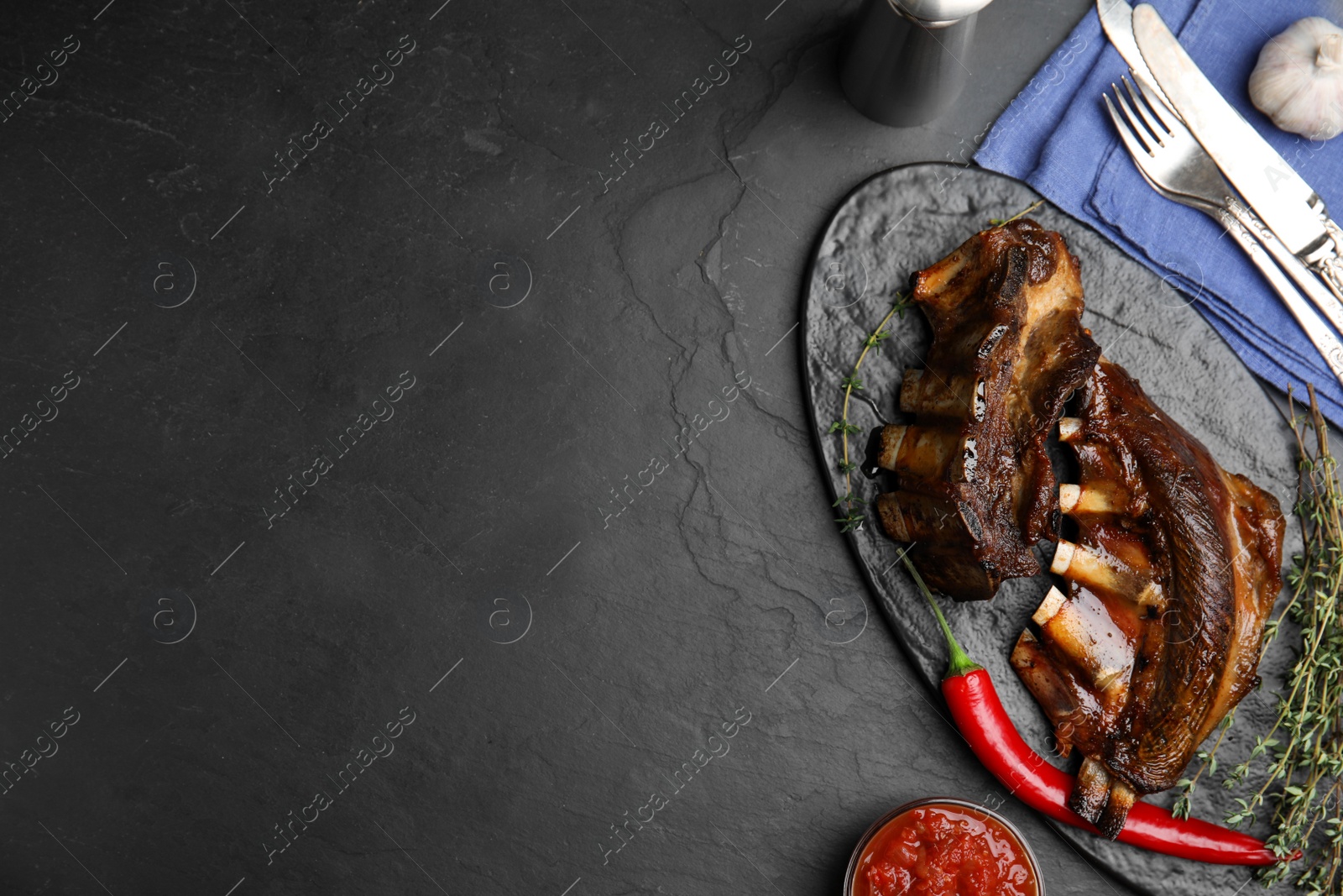 Photo of Delicious roasted ribs served on black table, flat lay. Space for text