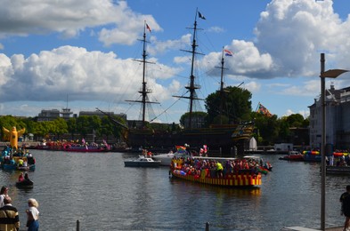 Photo of AMSTERDAM, NETHERLANDS - AUGUST 06, 2022: Boats with people holding LGBT pride flags at parade on river