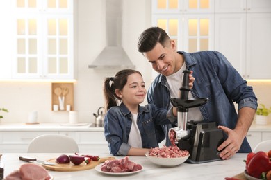 Photo of Father and daughter using modern meat grinder in kitchen. Space for text