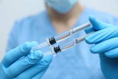 Doctor holding syringes with COVID-19 vaccine on light background, closeup