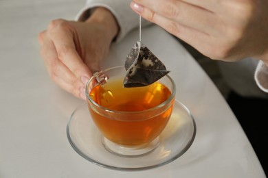 Photo of Woman taking tea bag out of cup at table, closeup