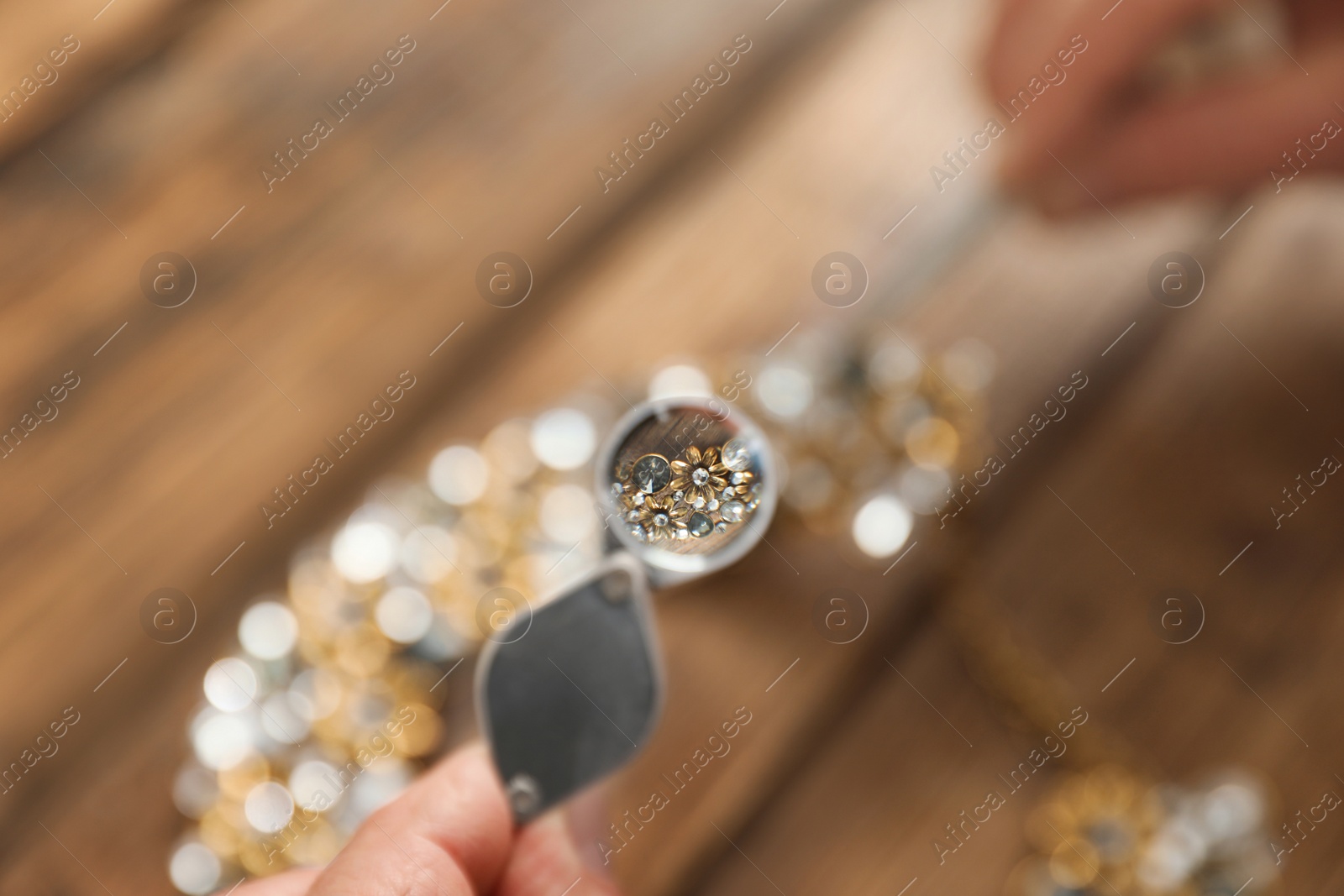 Photo of Male jeweler evaluating necklace at table in workshop, closeup view through magnifier
