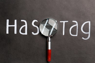 Photo of Magnifying glass and word Hashtag with symbol written on black background, top view