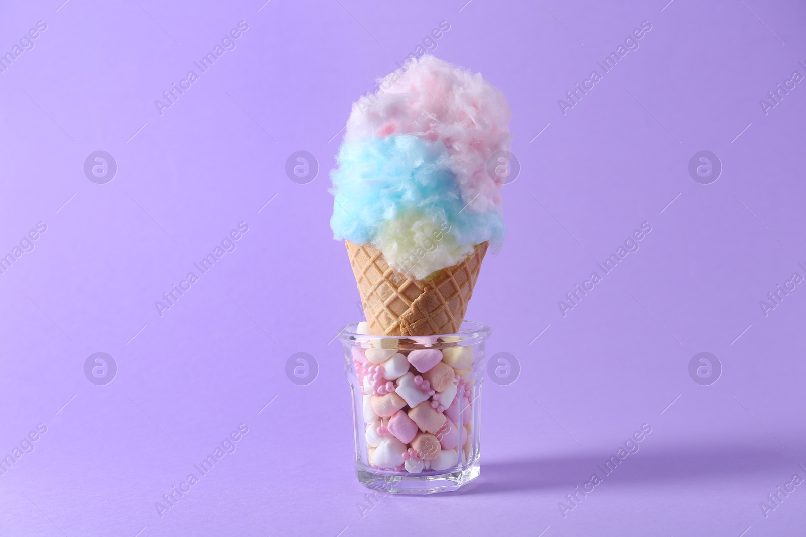 Photo of Sweet cotton candy in waffle cone on purple background