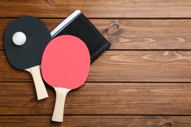 Photo of Ping pong rackets, net and ball on wooden table, flat lay. Space for text