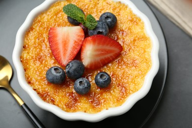 Delicious creme brulee with berries and mint in bowl on grey table, above view