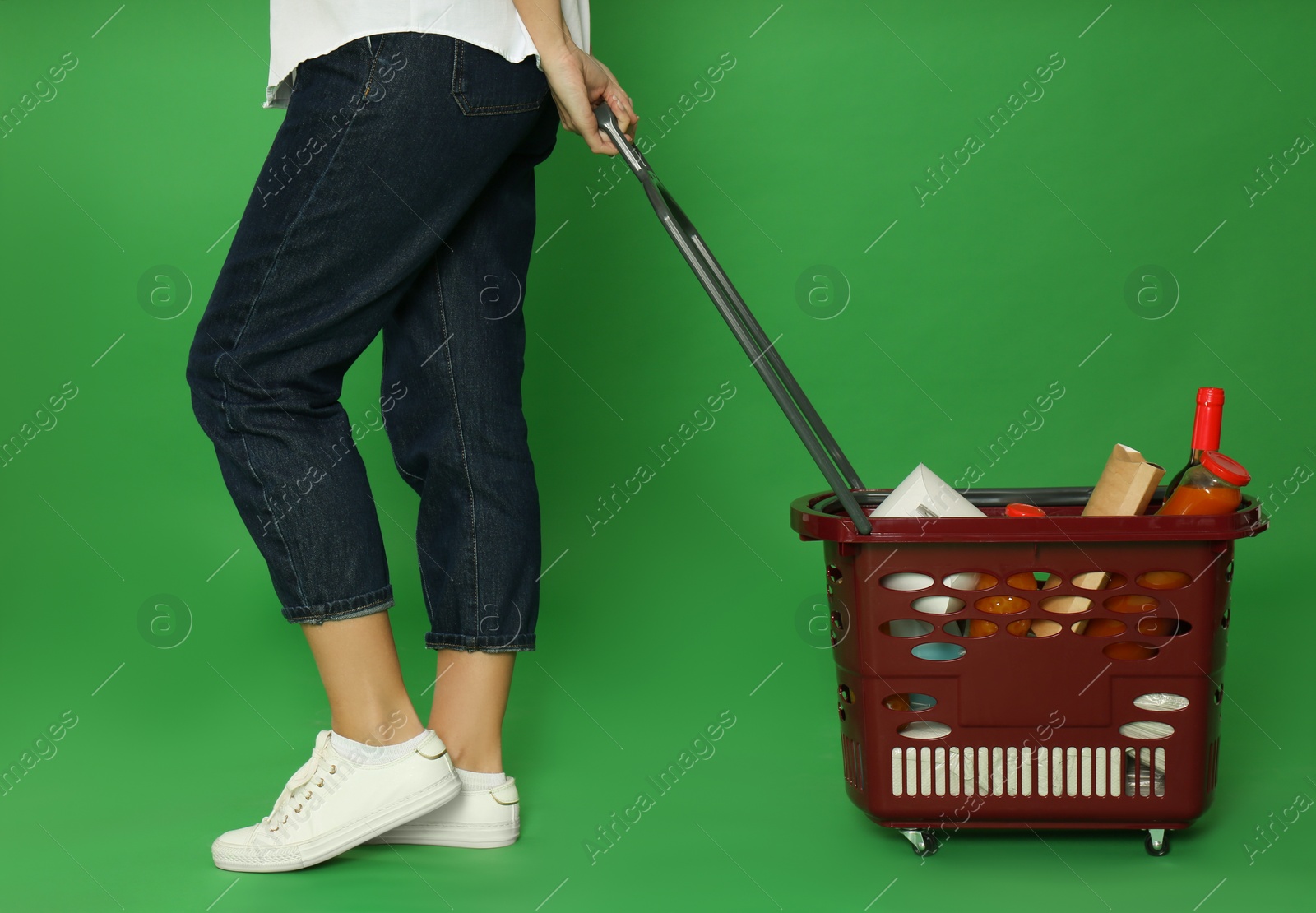 Photo of Woman with shopping basket full of different products on green background, closeup