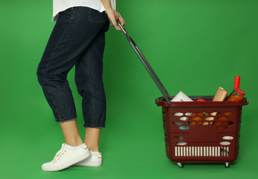 Woman with shopping basket full of different products on green background, closeup