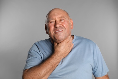 Photo of Mature man suffering from throat pain on light grey background
