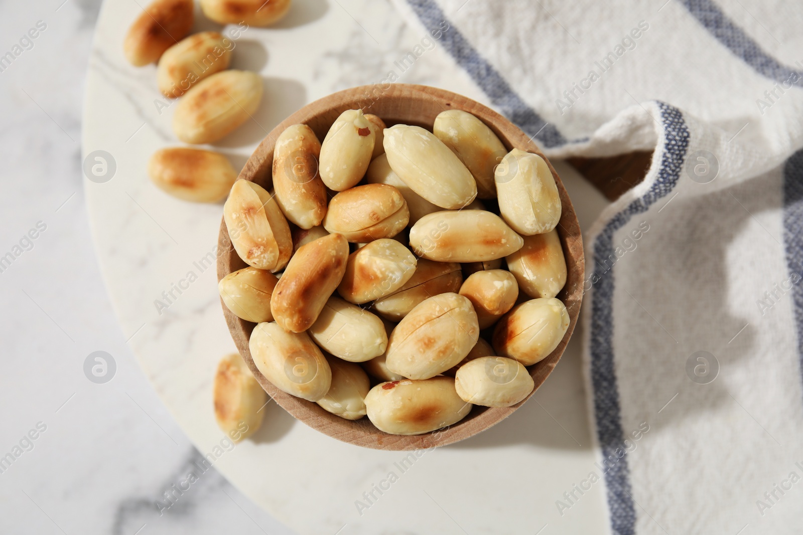 Photo of Roasted peanuts in bowl on white marble table, top view