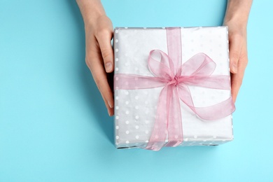 Photo of Young woman holding beautiful gift box on color background, top view