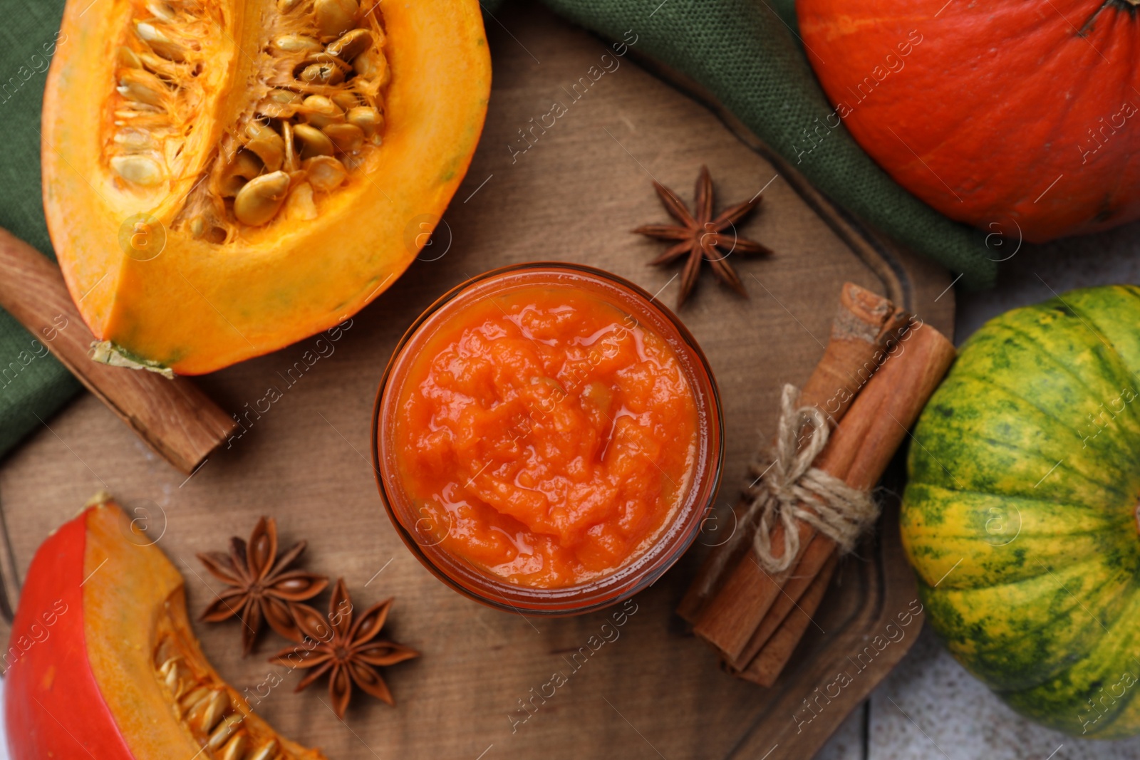Photo of Jar of delicious pumpkin jam and ingredients on wooden board, flat lay