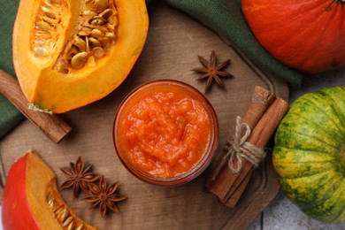 Photo of Jar of delicious pumpkin jam and ingredients on wooden board, flat lay