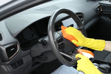 Woman cleaning steering wheel with rag in car, closeup