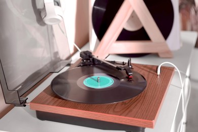 Image of Stylish turntable with vinyl disc and headphones on white chest of drawers at home