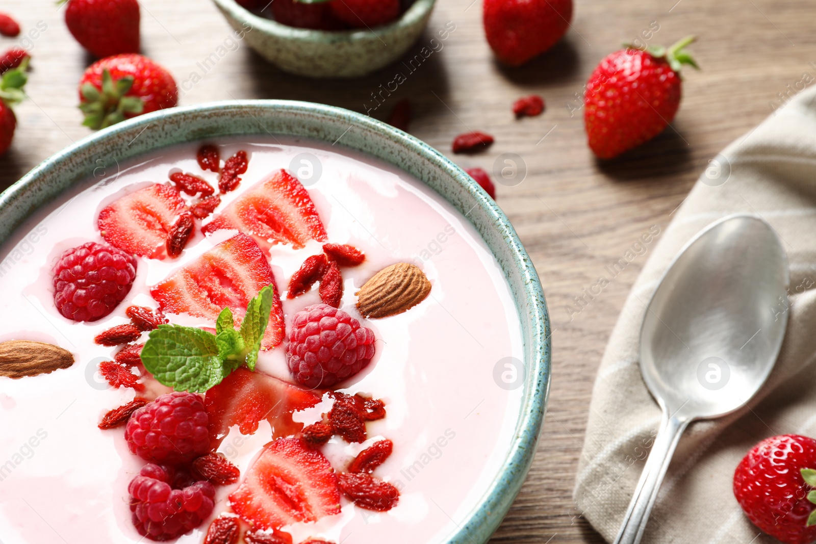 Photo of Smoothie bowl with goji berries and spoon on wooden table, closeup