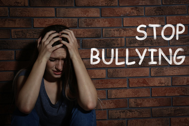Image of Message STOP BULLYING and abused teen girl crying near brick wall