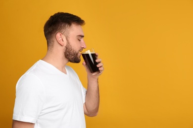 Photo of Handsome man with cold kvass on yellow background, space for text. Traditional Russian summer drink