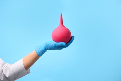Photo of Doctor holding pink enema on light blue background, closeup