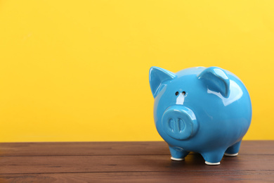 Photo of Blue piggy bank on wooden table against yellow background. Space for text