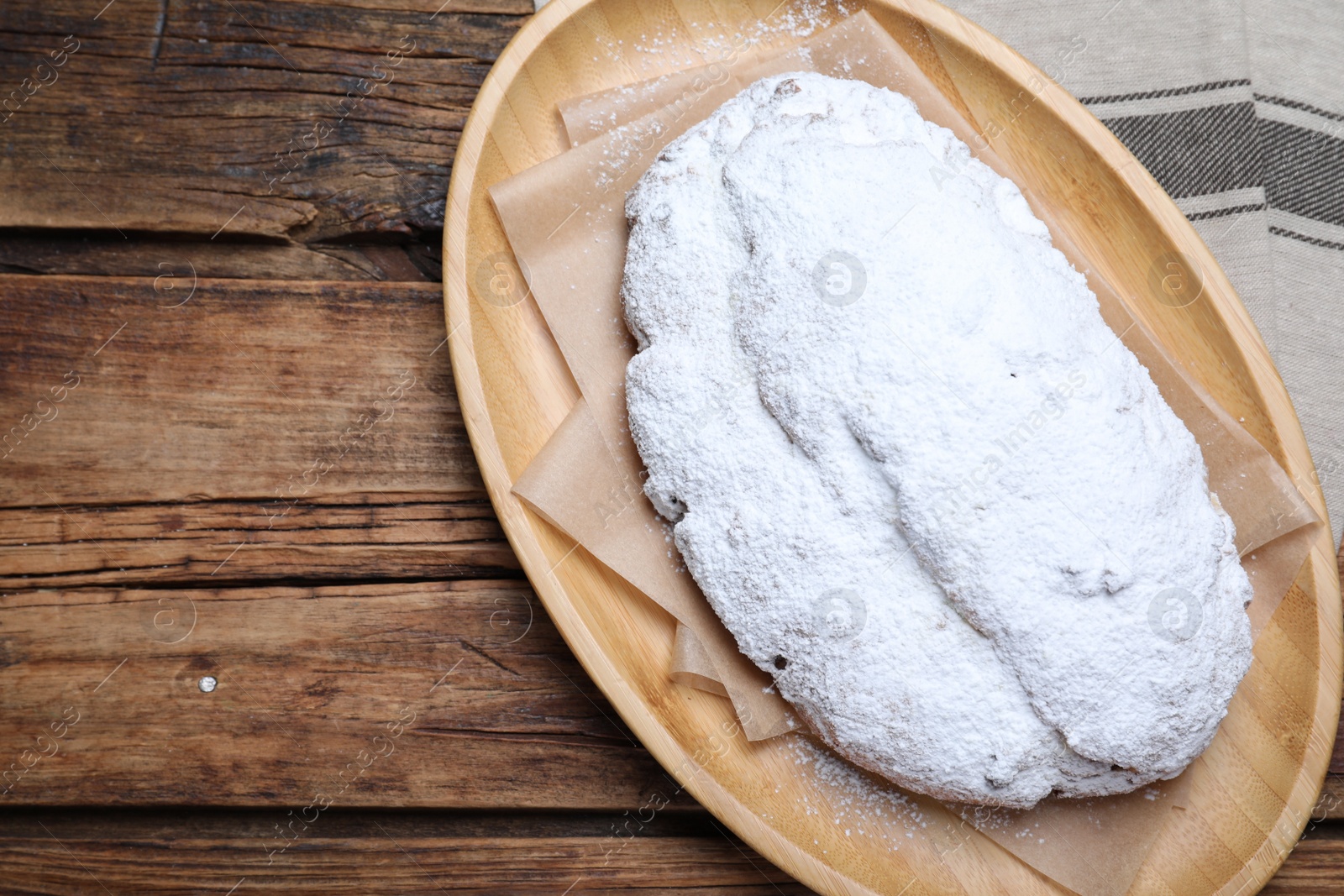 Photo of Plate of delicious Stollen sprinkled with powdered sugar on wooden table, top view. Space for text