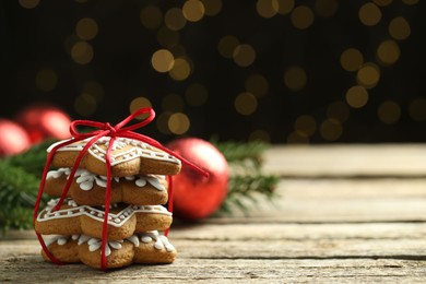 Photo of Tasty Christmas cookies with icing on wooden table against blurred lights. Space for text