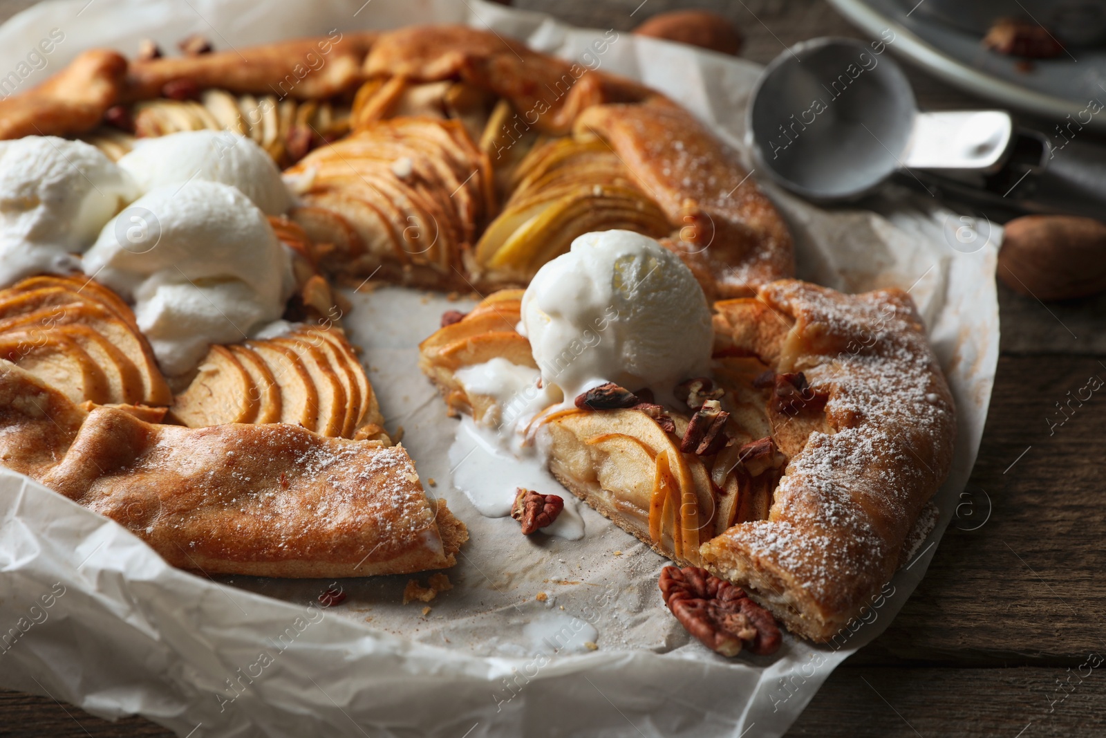 Photo of Delicious apple galette served with ice cream on wooden table, closeup